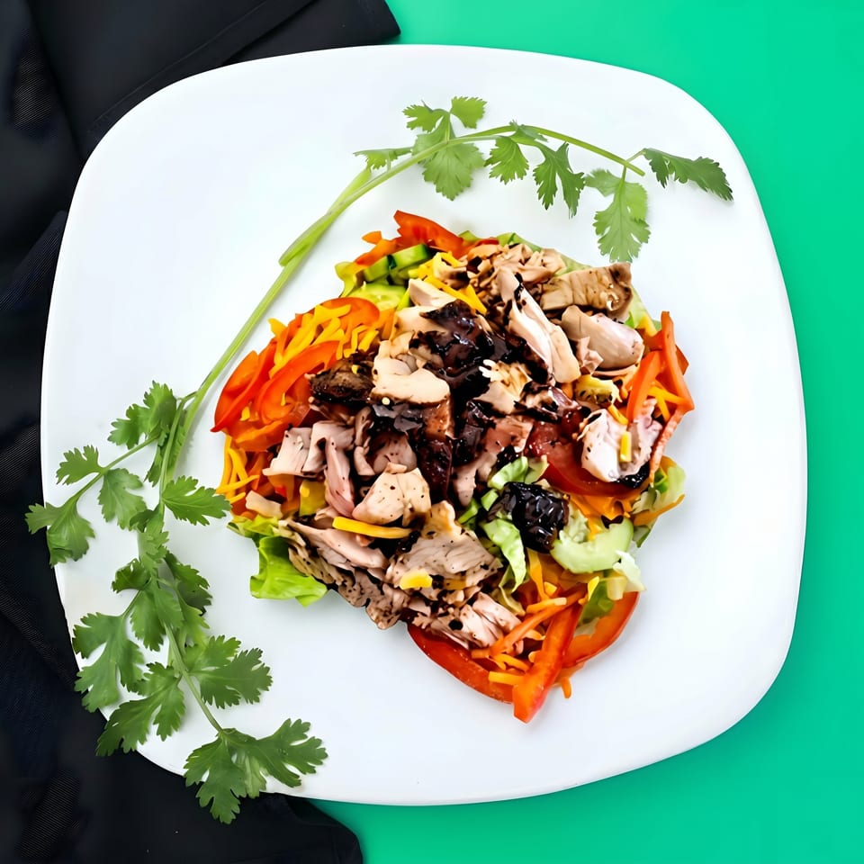 A vibrant salad with chicken, bell peppers, shredded carrots, and cilantro on a white plate.
