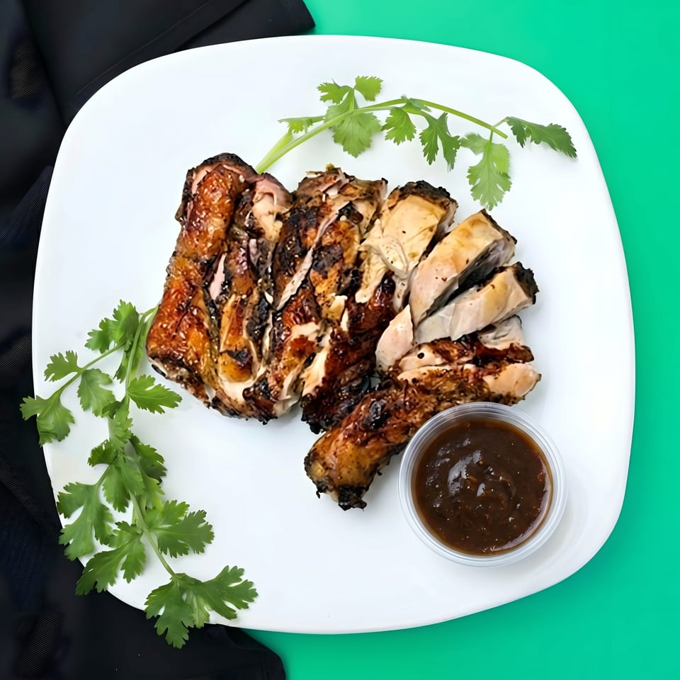 Grilled jerk chicken pieces with cilantro and a side of dark sauce on a white plate.