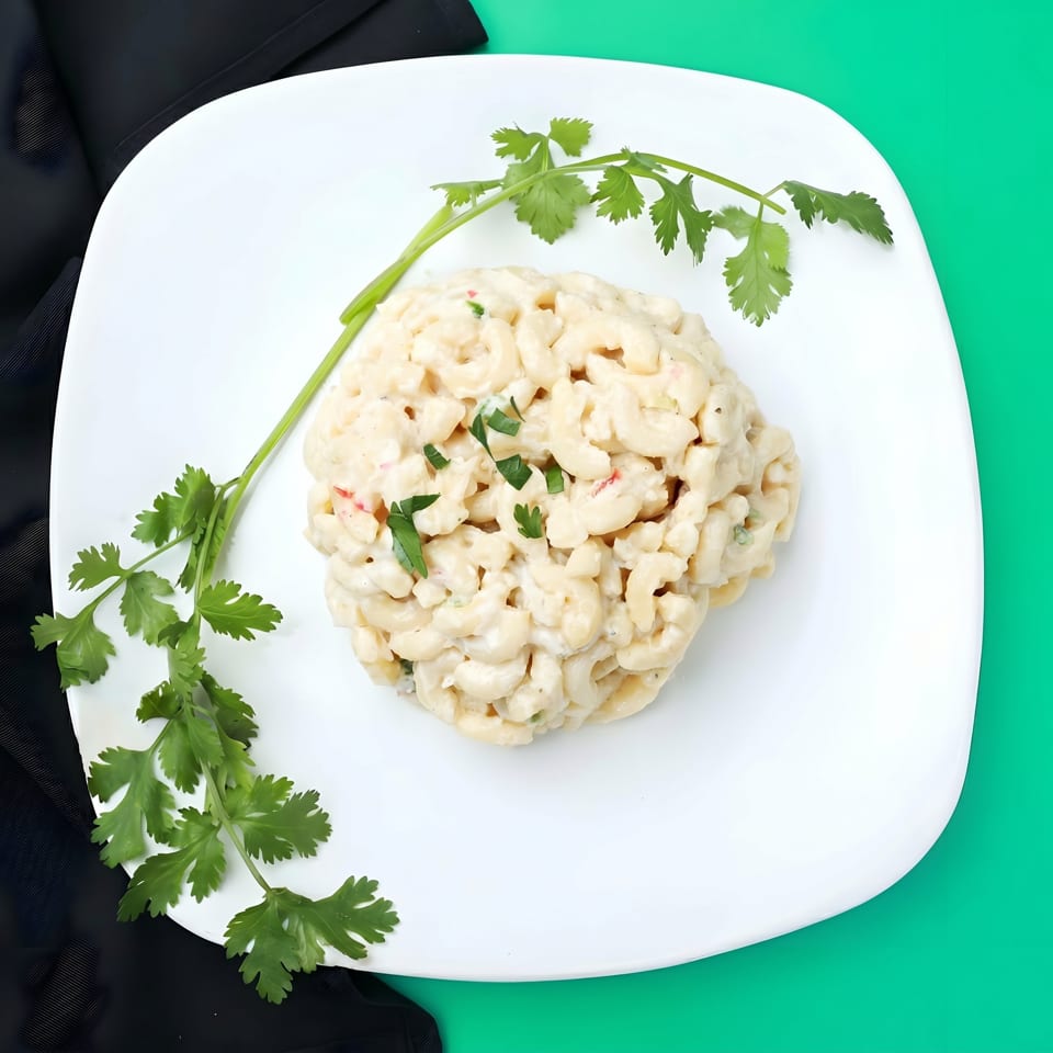 Creamy macaroni and cheese, garnished with fresh cilantro, on a white plate with a green background.