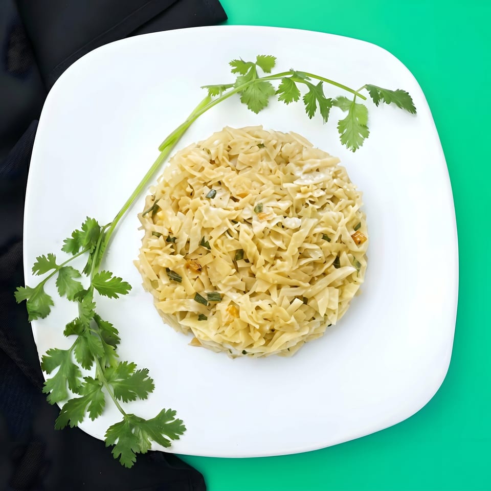Flat noodles with green onions and cilantro on a white plate, against a green and black background.